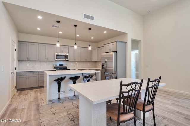 kitchen featuring pendant lighting, a breakfast bar area, an island with sink, light hardwood / wood-style floors, and stainless steel appliances