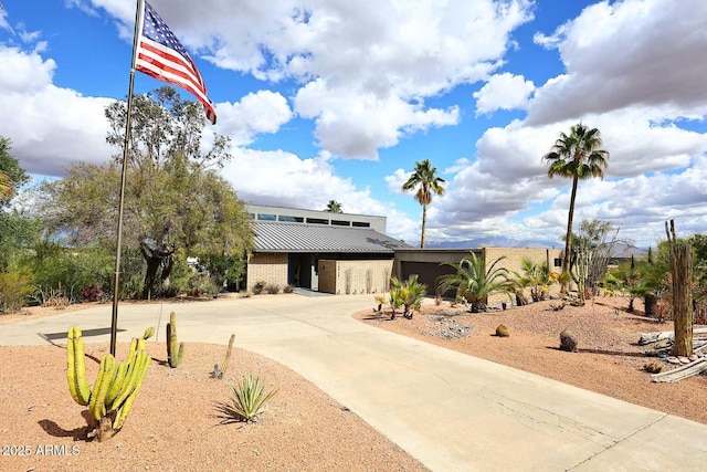 mid-century modern home with metal roof, an attached garage, brick siding, driveway, and a standing seam roof