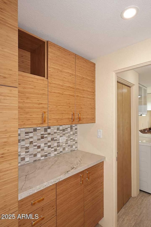 kitchen featuring tasteful backsplash, a textured ceiling, light stone countertops, washer / dryer, and light wood-type flooring