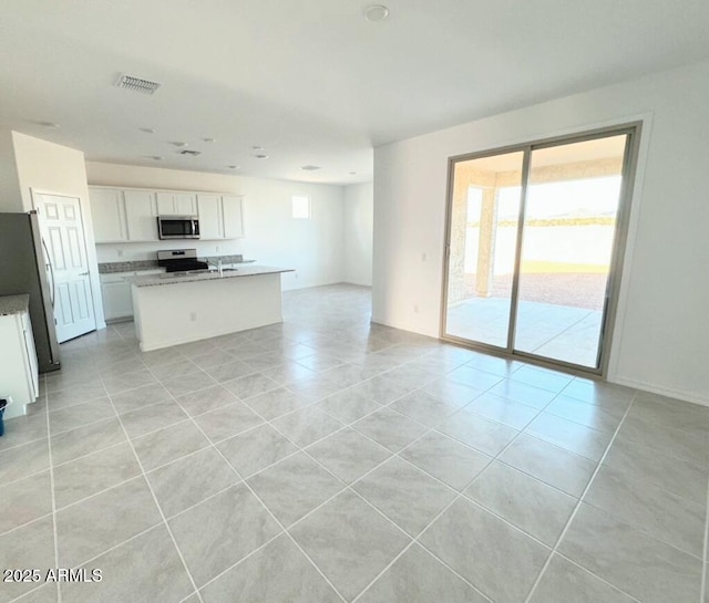 kitchen with appliances with stainless steel finishes, plenty of natural light, white cabinets, and a center island with sink