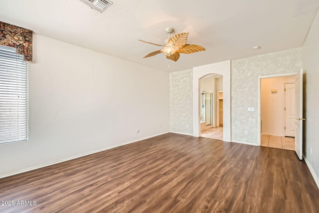 unfurnished bedroom with arched walkways, visible vents, ensuite bath, wood finished floors, and baseboards