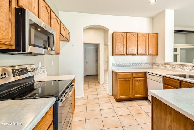 kitchen featuring arched walkways, light tile patterned floors, light countertops, appliances with stainless steel finishes, and a sink