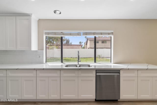 kitchen with light stone counters, decorative backsplash, white cabinets, and a sink