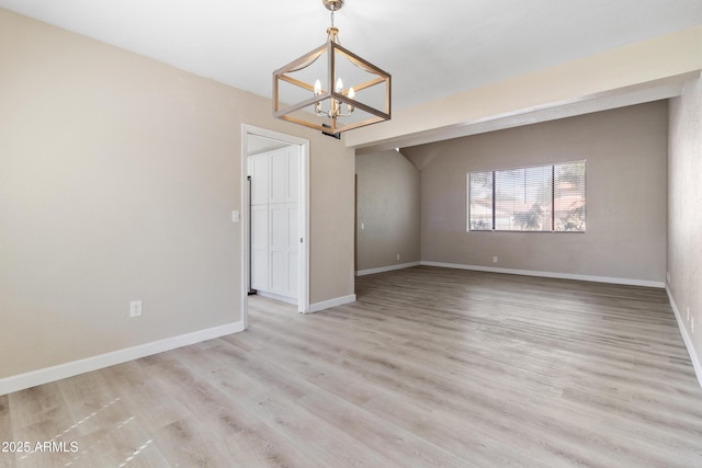 spare room featuring a notable chandelier, light wood-type flooring, and baseboards