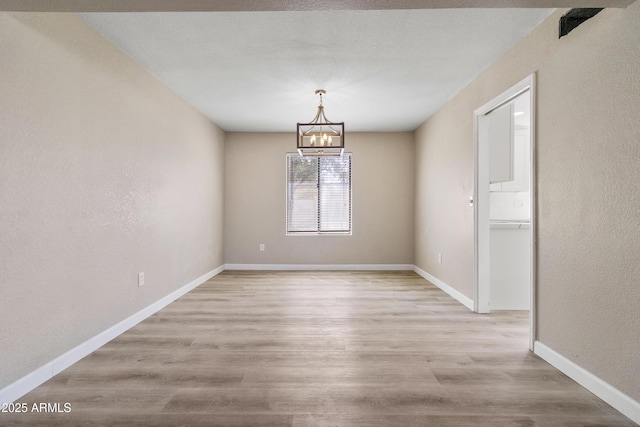 empty room featuring a notable chandelier, baseboards, light wood-style floors, and a textured wall