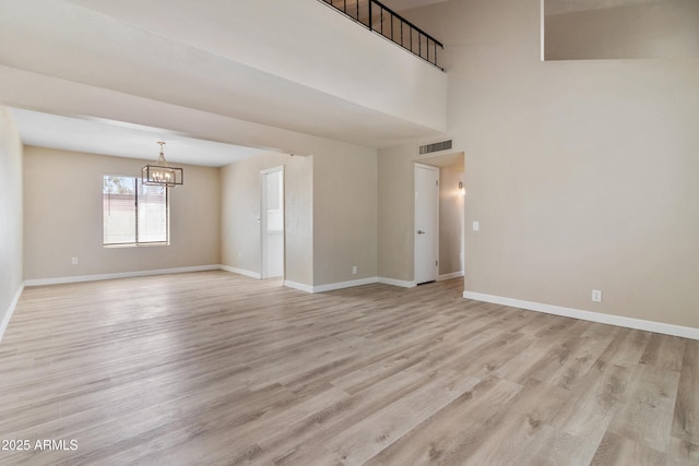 spare room featuring light wood finished floors, visible vents, baseboards, and an inviting chandelier