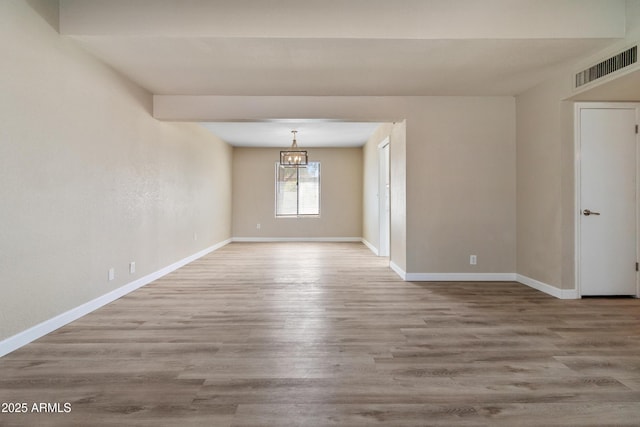 spare room with visible vents, baseboards, wood finished floors, and a chandelier