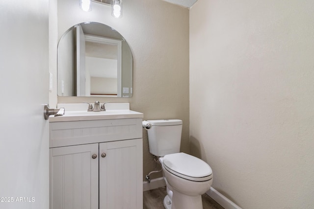 bathroom featuring baseboards, toilet, wood finished floors, and vanity