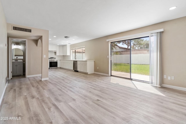 unfurnished living room with a sink, visible vents, baseboards, and light wood finished floors