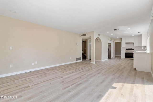 unfurnished living room featuring visible vents, baseboards, light wood finished floors, recessed lighting, and arched walkways