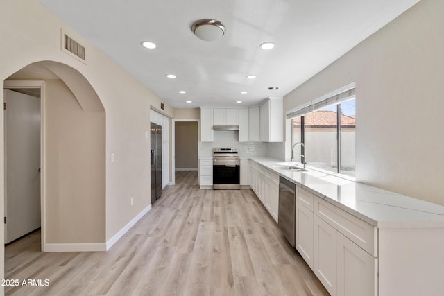 kitchen with visible vents, light wood-style flooring, a sink, under cabinet range hood, and appliances with stainless steel finishes