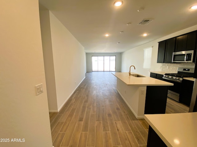 kitchen featuring visible vents, light wood-style flooring, appliances with stainless steel finishes, a sink, and dark cabinets