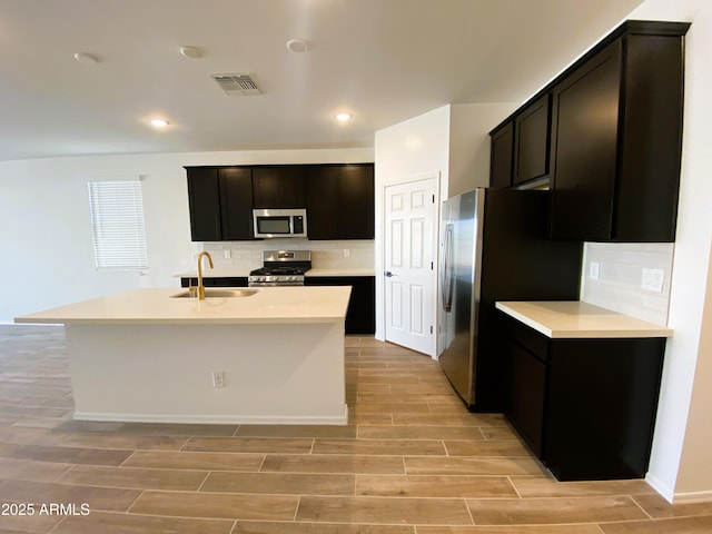 kitchen with a kitchen island with sink, stainless steel appliances, a sink, and wood finish floors