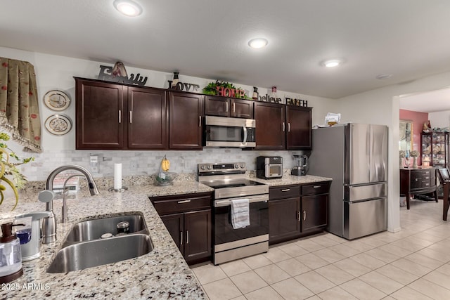 kitchen with a sink, appliances with stainless steel finishes, light tile patterned flooring, decorative backsplash, and dark brown cabinets