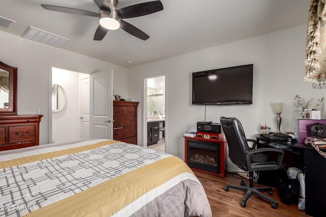 bedroom featuring ceiling fan, visible vents, ensuite bath, and wood finished floors