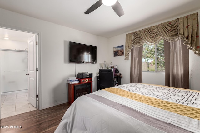 bedroom with baseboards, ensuite bath, ceiling fan, and wood finished floors