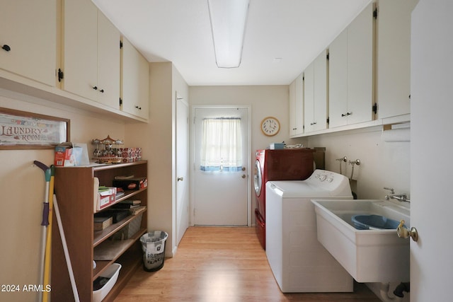 clothes washing area with a sink, light wood-style flooring, washing machine and dryer, and cabinet space