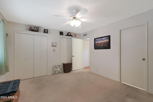 unfurnished bedroom featuring a textured ceiling, carpet flooring, visible vents, a ceiling fan, and multiple closets