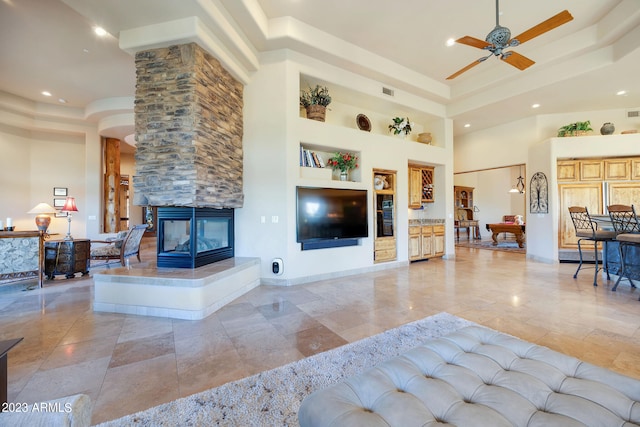 living room with a tray ceiling, ceiling fan, a fireplace, and a high ceiling