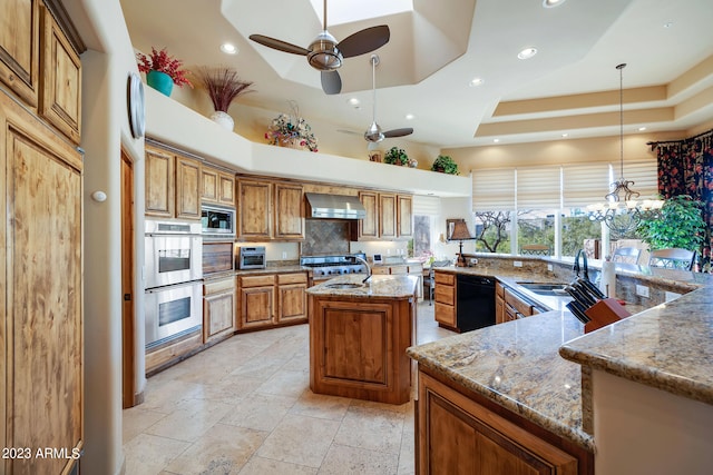 kitchen featuring a large island, wall chimney exhaust hood, pendant lighting, a tray ceiling, and appliances with stainless steel finishes