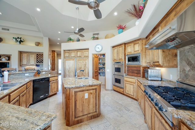 kitchen featuring sink, wall chimney exhaust hood, stainless steel appliances, light stone counters, and a kitchen island with sink