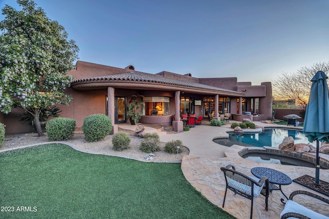 back house at dusk featuring a pool with hot tub and a patio area