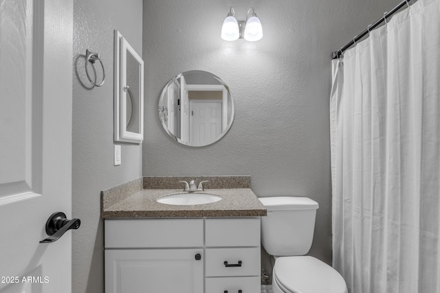bathroom featuring toilet, a textured wall, and vanity