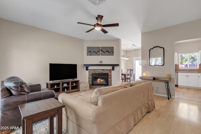 living room with a ceiling fan, visible vents, a stone fireplace, and light wood-style flooring