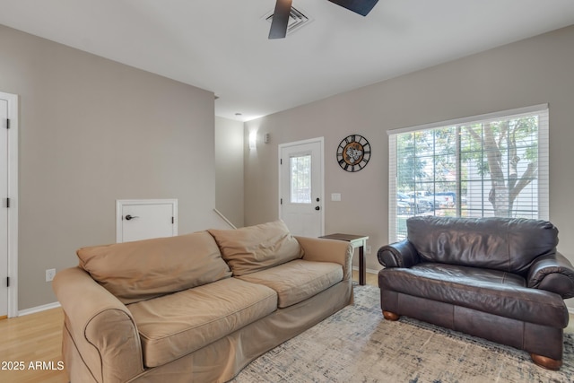 living room featuring baseboards, a ceiling fan, light wood finished floors, and visible vents