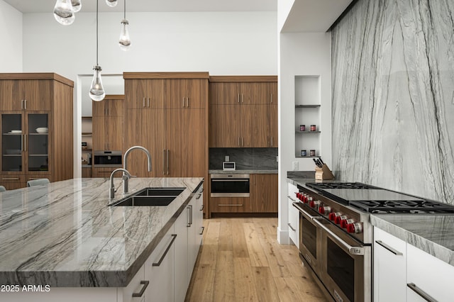 kitchen featuring sink, white cabinets, hanging light fixtures, double oven range, and a center island with sink