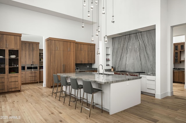 kitchen featuring light hardwood / wood-style flooring, a breakfast bar, hanging light fixtures, a high ceiling, and light stone counters