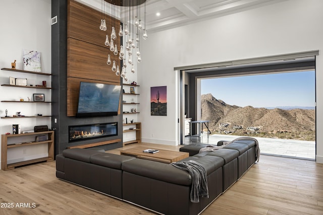 living room featuring beamed ceiling, a towering ceiling, coffered ceiling, and light hardwood / wood-style flooring