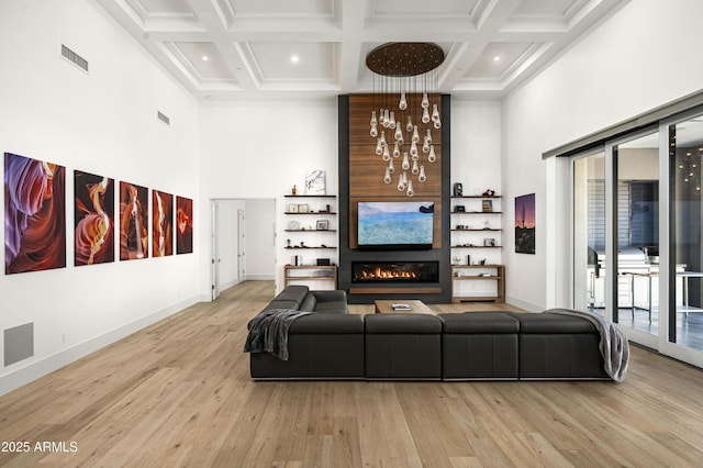 living room featuring a high ceiling, a large fireplace, a chandelier, and light hardwood / wood-style floors