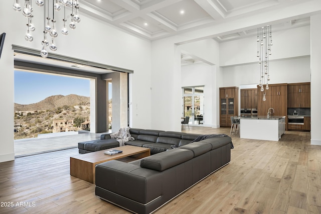 living room featuring a towering ceiling, coffered ceiling, light hardwood / wood-style floors, a mountain view, and beam ceiling