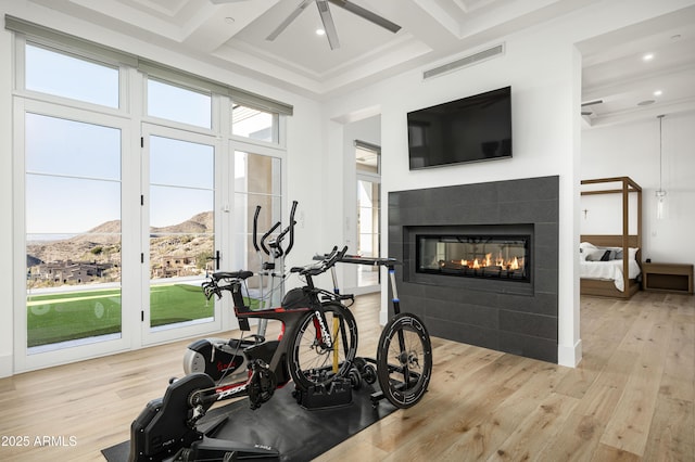 workout area with coffered ceiling, a fireplace, light hardwood / wood-style flooring, and ceiling fan