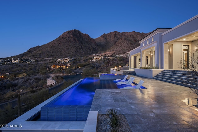 pool at dusk with a mountain view, a patio area, and a hot tub