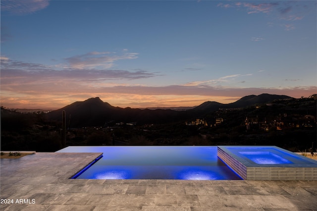 pool at dusk with an in ground hot tub, a mountain view, and a patio