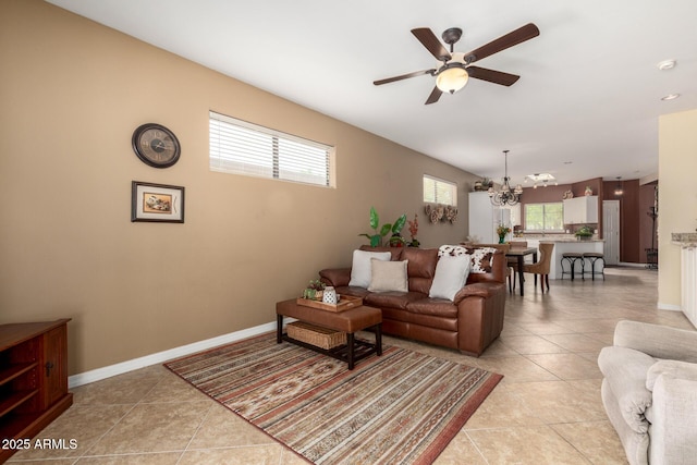 living area featuring light tile patterned floors, baseboards, and ceiling fan with notable chandelier