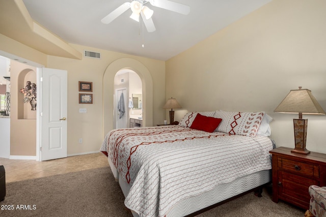 carpeted bedroom featuring ensuite bathroom, visible vents, ceiling fan, arched walkways, and baseboards