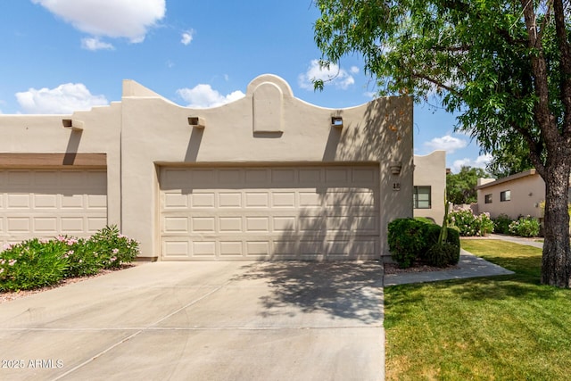 pueblo-style house featuring concrete driveway, a front yard, stucco siding, and a garage