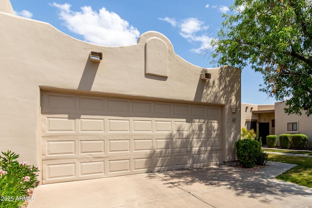 pueblo-style home with a garage, stucco siding, and driveway