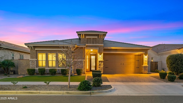 prairie-style home with a garage, stone siding, fence, decorative driveway, and a front yard