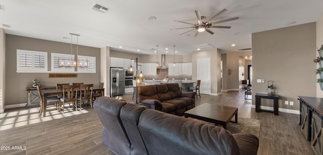 living room featuring ceiling fan with notable chandelier, visible vents, baseboards, and wood finished floors