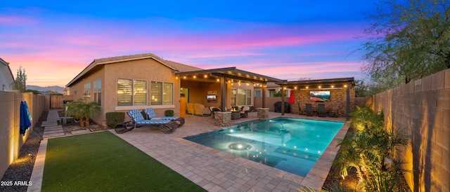 pool at dusk featuring a hot tub, a fenced backyard, and a patio