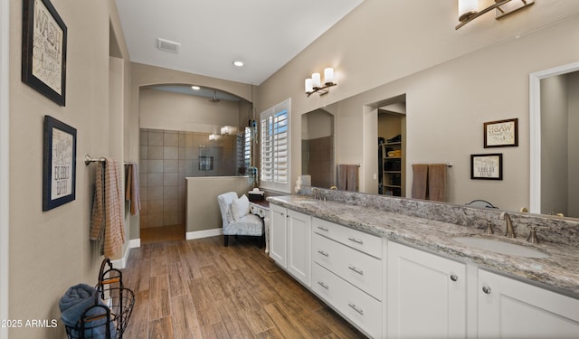 bathroom featuring wood finished floors, a sink, visible vents, double vanity, and walk in shower