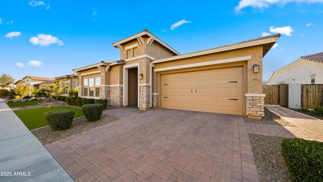 view of front of property with decorative driveway, stucco siding, an attached garage, fence, and stone siding