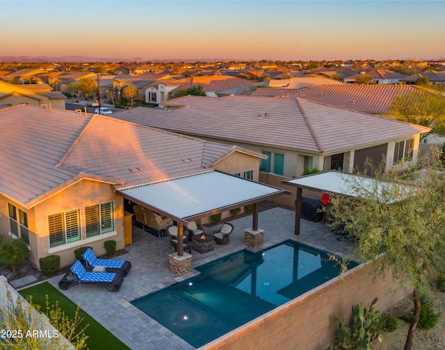 pool at dusk featuring a fenced backyard, a residential view, outdoor dry bar, and a patio