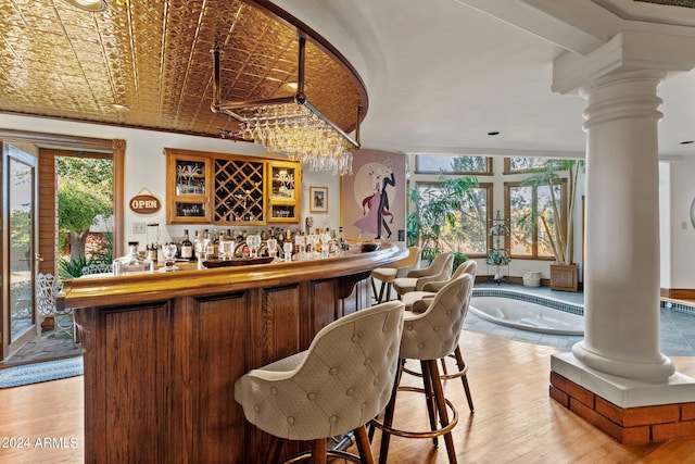 bar with a chandelier, ornate columns, and light hardwood / wood-style flooring