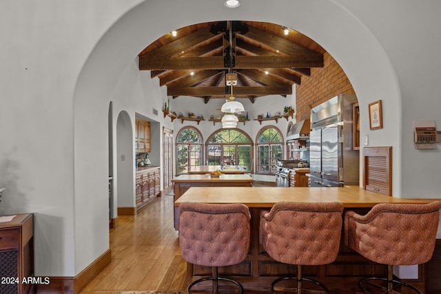 kitchen featuring wood counters, high end fridge, vaulted ceiling with beams, and light hardwood / wood-style flooring