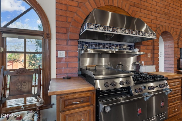 kitchen with wooden counters, brick wall, and wall chimney exhaust hood